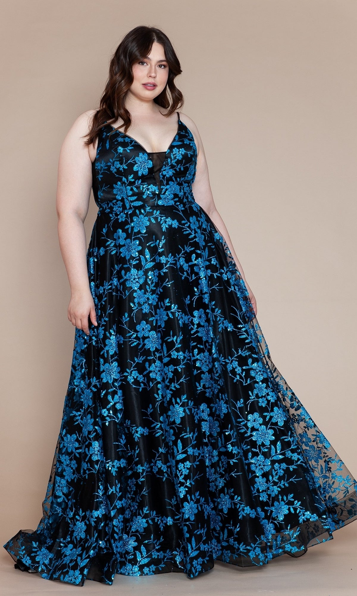 A woman wears the Poly USA W1134 Plus-Size Long Glitter Prom Gown, featuring blue floral patterns, and stands against a plain beige background.